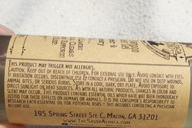 Hand holding a cylindrical product with a label on a sandy surface