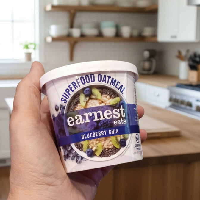 Hand holding a container of Earnest Superfood Oatmeal on a dark countertop