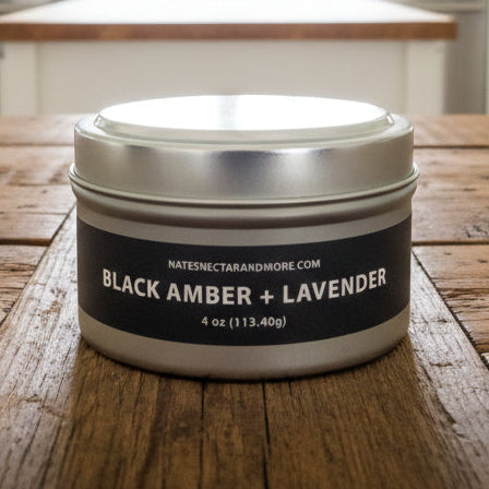 Candle tin labeled 'Black Amber + Lavender' on a surface with a book titled 'Expedition' by Lee Child.