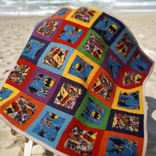 Colorful quilt with superhero patterns on a beach chair by the ocean.