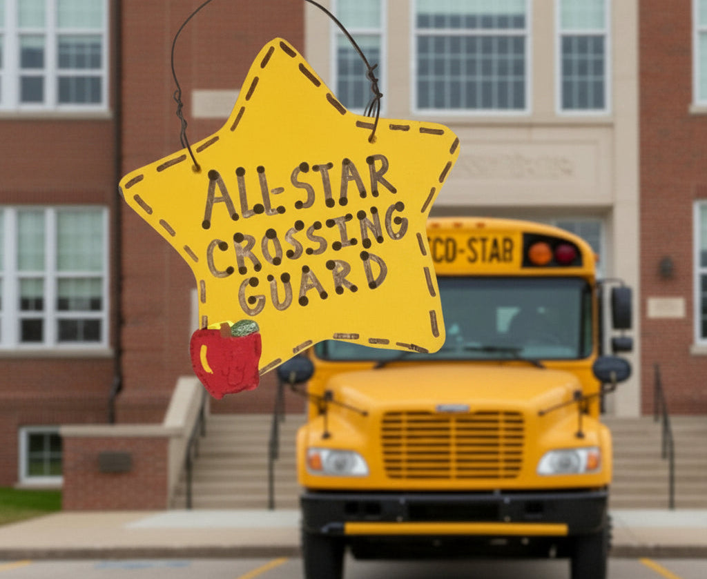 Hand holding a 'All-Star Crossing Guard' sign in front of a school bus with a school building in the background.