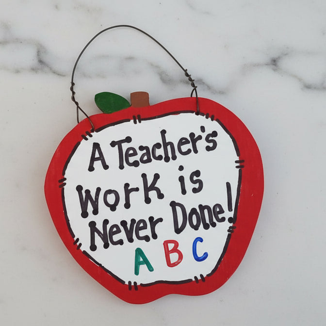 Decorative apple-shaped sign with 'A Teacher's Work is Never Done! ABC' text on a marble background