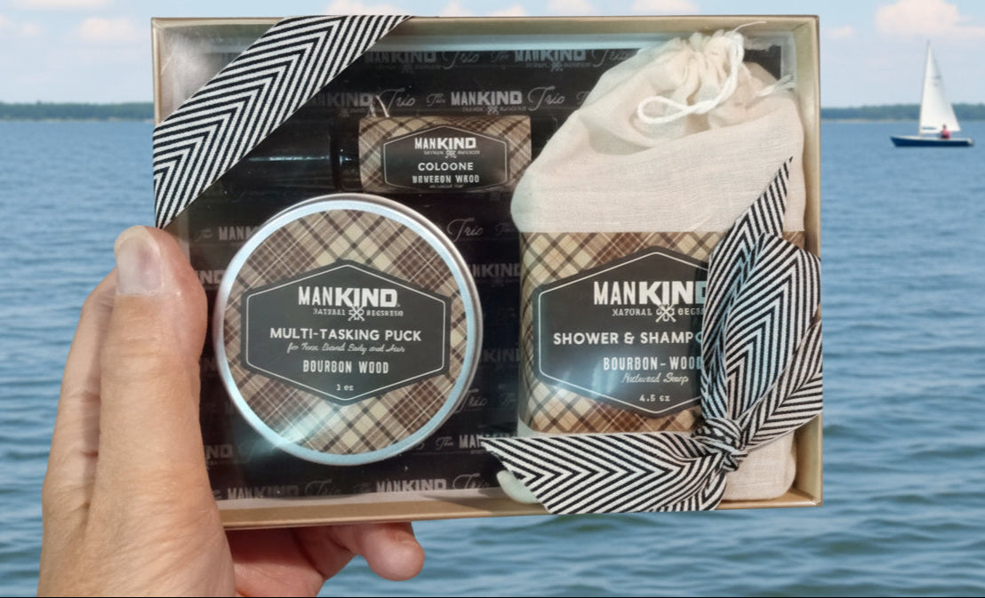 Manking grooming kit held over a scenic lake with a sailboat.