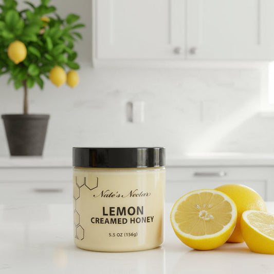 Jar of 'Lemon Creamed Honey' on a kitchen counter with lemons and a plant in the background.